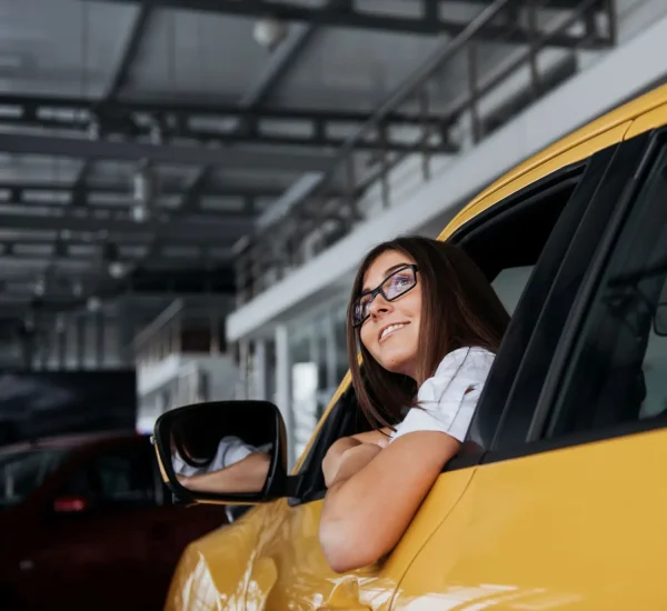 smiling-woman-inside-a-yellow-car-looking-up-2026-01-09-00-39-43-utc.webp